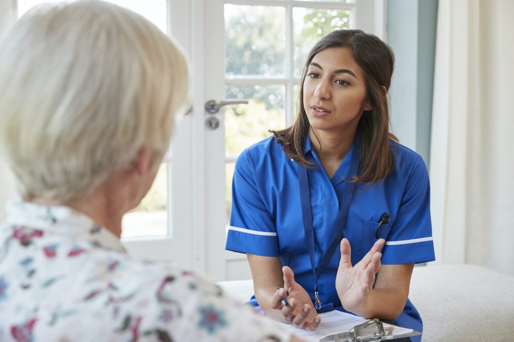 Senior woman talking to young care nurse on home visit