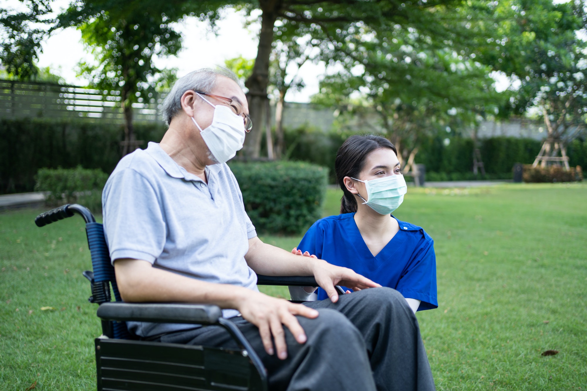 Asian nurse wear mask, support disabled senior elder man on wheelchair at green park