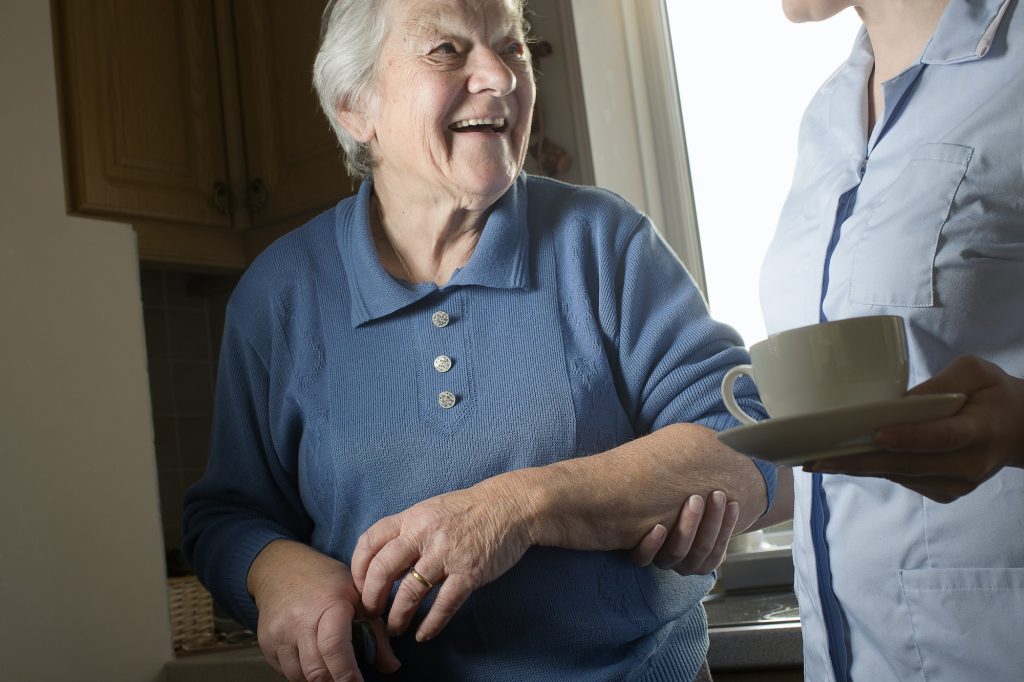 Personal care assistant carrying cup of tea for senior woman